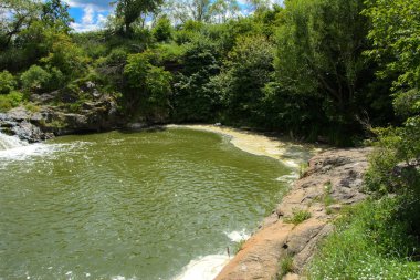 Yoluyla ve liken ve moss bir arka plan mavi bir gökyüzü ve yeşil bitki örtüsü ile kaplı kaya şelale Nehri akar.