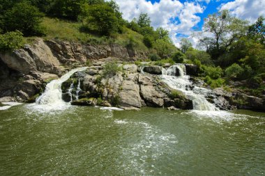 Yoluyla ve liken ve moss bir arka plan mavi bir gökyüzü ve yeşil bitki örtüsü ile kaplı kaya şelale Nehri akar.