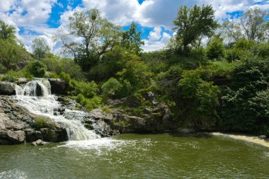 Yoluyla ve liken ve moss bir arka plan mavi bir gökyüzü ve yeşil bitki örtüsü ile kaplı kaya şelale Nehri akar.