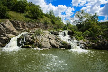 Yoluyla ve liken ve moss bir arka plan mavi bir gökyüzü ve yeşil bitki örtüsü ile kaplı kaya şelale Nehri akar.