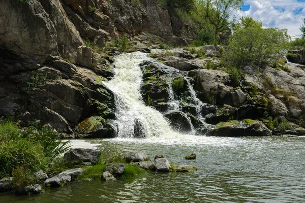 Yoluyla ve liken ve moss bir arka plan mavi bir gökyüzü ve yeşil bitki örtüsü ile kaplı kaya şelale Nehri akar.