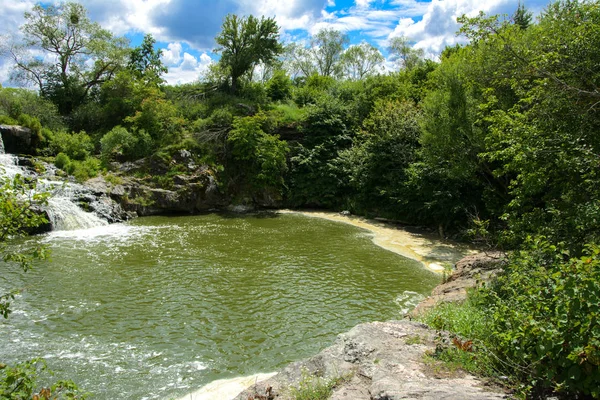 川にある滝の流れと苔と緑と青い空を背景に苔に覆われた岩の上 — ストック写真