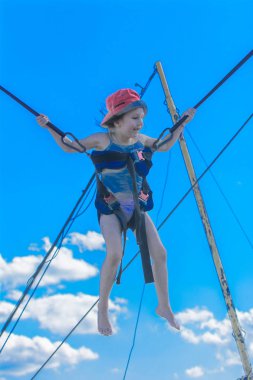 Kauçuk halatlar mavi gökyüzü ile bir trambolin üzerinde atlama çocuk. Macera ve doğa sporları. Yaz eğlence, Zıplama kavramı.