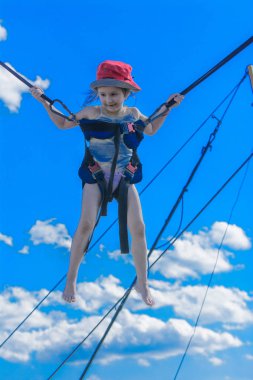 Kauçuk halatlar mavi gökyüzü ile bir trambolin üzerinde atlama çocuk. Macera ve doğa sporları. Yaz eğlence, Zıplama kavramı.