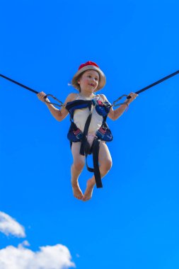 Kauçuk halatlar mavi gökyüzü ile bir trambolin üzerinde atlama çocuk. Macera ve doğa sporları. Yaz eğlence, Zıplama kavramı.