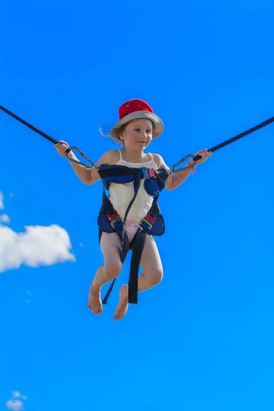 Children jumping on a trampoline with rubber ropes against the blue sky. Adventure and extreme sports. The concept of summer recreation, jumping.