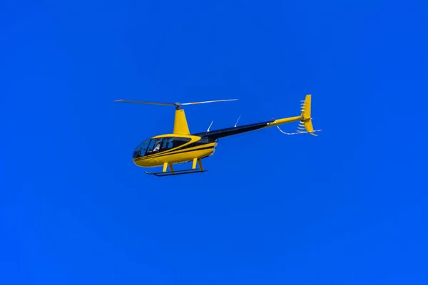 黄色私人直升机在明亮的蓝天背景下飞行 有一名机组人员参与 在下面射击 与乌克兰国旗的联系 — 图库照片