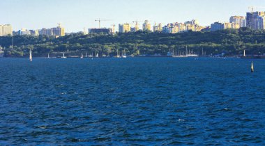 Muhteşem panorama, denizden görünümüne yumuşak güneş ışığı altında gün batımına şehrin kıyı şeridi. Yüksek katlı binalar ve sahilde ticari yapılar