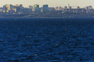 Muhteşem panorama, denizden görünümüne yumuşak güneş ışığı altında gün batımına şehrin kıyı şeridi. Yüksek katlı binalar ve sahilde ticari yapılar