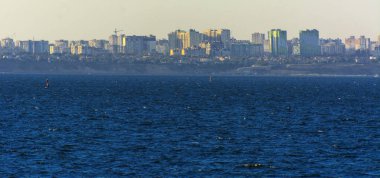 Muhteşem panorama, denizden görünümüne yumuşak güneş ışığı altında gün batımına şehrin kıyı şeridi. Yüksek katlı binalar ve sahilde ticari yapılar