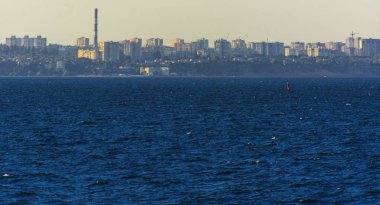 Muhteşem panorama, denizden görünümüne yumuşak güneş ışığı altında gün batımına şehrin kıyı şeridi. Yüksek katlı binalar ve sahilde ticari yapılar