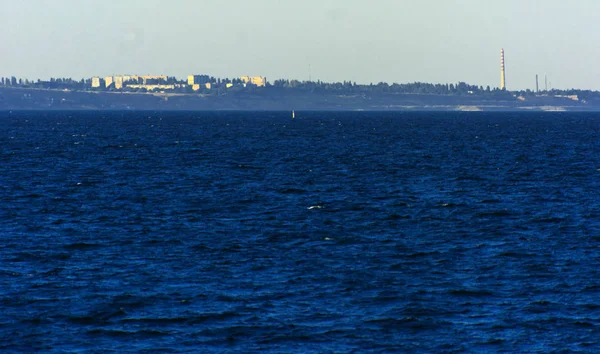 Muhteşem panorama, denizden görünümüne yumuşak güneş ışığı altında gün batımına şehrin kıyı şeridi. Yüksek katlı binalar ve sahilde ticari yapılar