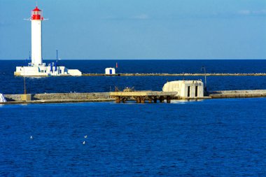 Denizin yumuşak renkler güzel akşam mavi gökyüzünde zemin karşı bağlantı noktasına girişinde bir deniz feneri. Yaz deniz manzarası. Bir kırmızı top ile beyaz deniz feneri. Karadeniz. Odessa Limanı