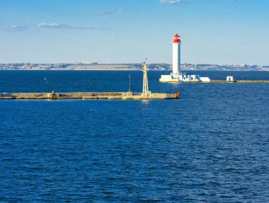 Denizin yumuşak renkler güzel akşam mavi gökyüzünde zemin karşı bağlantı noktasına girişinde bir deniz feneri. Yaz deniz manzarası. Bir kırmızı top ile beyaz deniz feneri. Karadeniz. Odessa Limanı