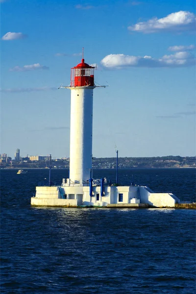 A lighthouse in the sea at the entrance to the port against the backdrop of a beautiful evening blue sky in soft colors. Summer seascape. White lighthouse with a red top. Black Sea. Seaport of Odessa