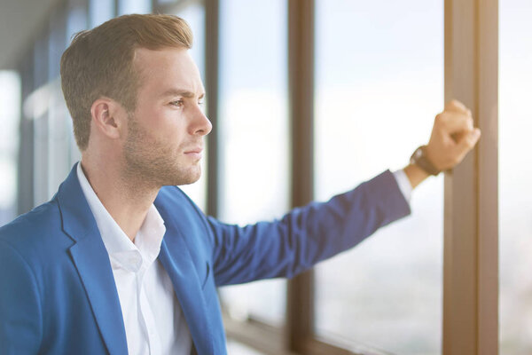 Self sufficiency in mind. Close up of a confident successful young businessman standing near window in his office while resting after work