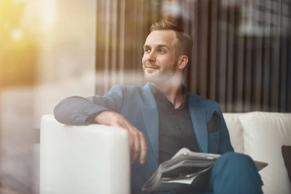 Enjoy every day of your life. Positive self assertive businessman holding a newspaper and sitting on the couch while resting in the office