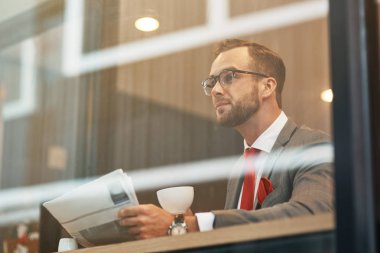 Bir uçak bekliyor. Bir gazete okuyor ve havaalanında dinlenme sırasında kahve içme çekici genç profesyonel iş adamı