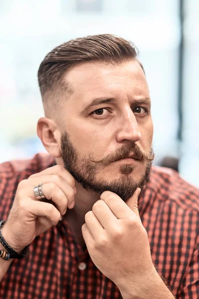 What a nice work. Portrait of a handsome young hipster showing his beard while sitting in the barbershop