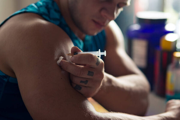 Daily habit. Close up of a professional bodybuilder making an injection at the table