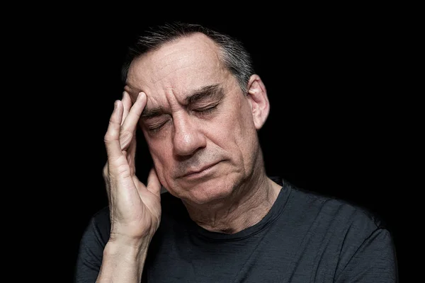 Closeup High Contrast Portrait of Stressed Unhappy Man with Hand to Face on Black Background