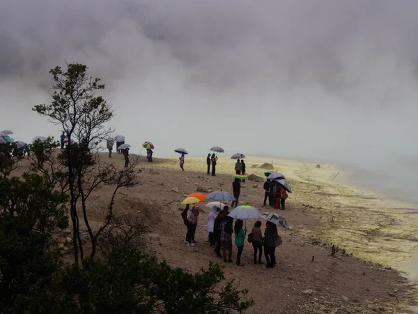 Pessoas e guarda-chuva em Kawah Putih é um lago de cratera impressionante e — Fotografia de Stock