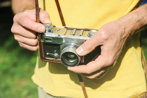 A man is holding a vintage camera. One of his hand is setting the lens.