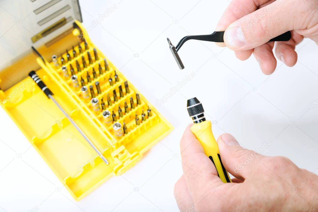 A man is using a tweezers to insert a bit into a screwdriver. Next there is a set of bits.