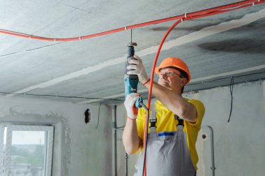 Bir elektrikçi bir tavan, bir perforator ile oluklu boru tamir için sondaj.