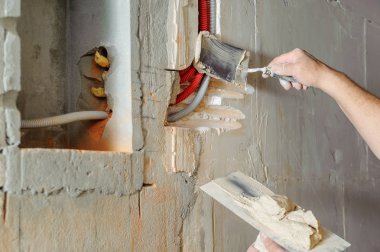 Bir işçi bir alçı ile malalar tutuyor. Duvardaki elektrik oluklu küçük borular koruyor.