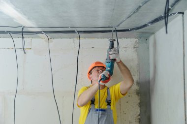 Bir elektrikçi bir tavan, bir perforator ile elektrik kablolarının düzeltmek için sondaj.