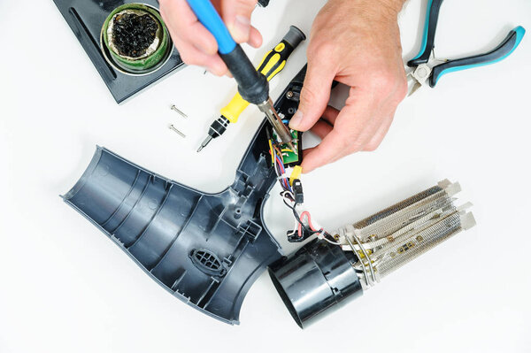 Hairdryer in a disassembled condition on a white background. The man is repairing it.