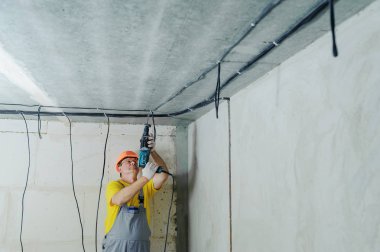Bir elektrikçi bir tavan, bir perforator ile elektrik kablolarının düzeltmek için sondaj.