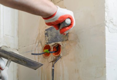 Bir işçi bir alçı ile malalar tutuyor. Duvardaki elektrik oluklu küçük borular koruyor.