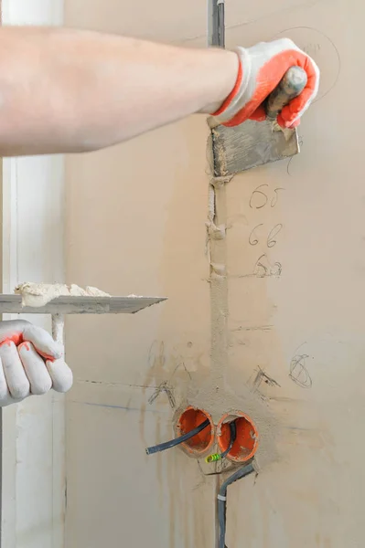 A worker is holding trowels with a gypsum. It is covering the electric corrugated tubes in the wall.