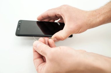 Bir adam bir smartphone tutuyor. SIM kart yuvasýný açmak için PIN kullanıyor.