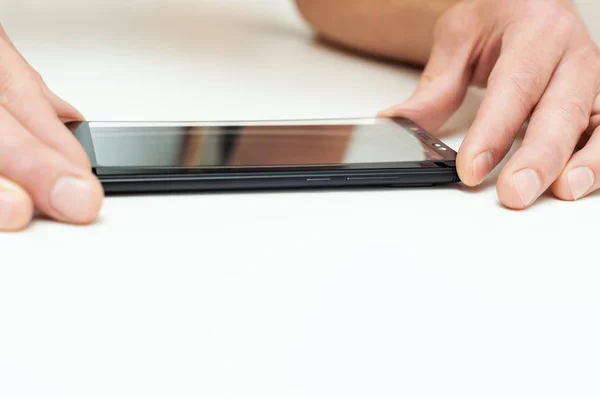 A man is glueing a protective glass on the screen of a smartphone.