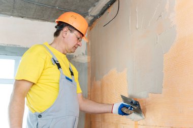 İşçi macun duvardaki bir fiberglas ağ üzerinde uyguluyor. O bir mala kullanıyor.