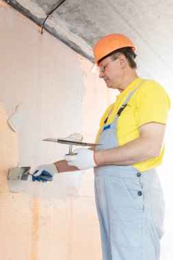 İşçi macun duvardaki bir fiberglas ağ üzerinde uyguluyor. O bir mala kullanıyor.