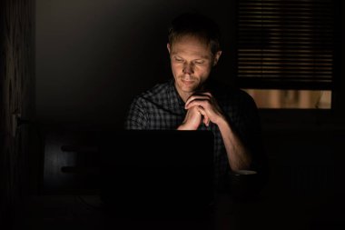 Adam gece iş yerinde bir dizüstü bilgisayar ekranına arıyor.