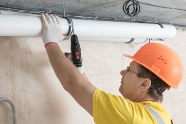 İşçi tavana bir tornavida ile havalandırma boruları tamir ediyor.