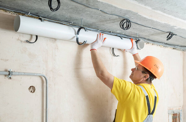 The worker is installing a ventilation system in the apartment.