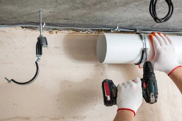 A worker is fixing ventilation pipes to the ceiling with a screwdriver.