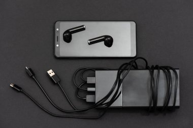 Bir akıllı telefon, bir kulaklık ve şarj kabloları güç bankayla karanlık bir arka plan üzerinde.