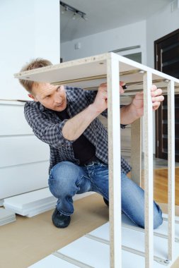 Adam evde mobilya montaj. O montaj ve komodinin kare bağlama.