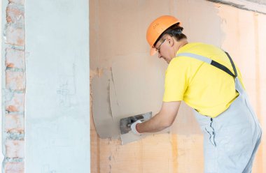 İşçi macun duvardaki bir fiberglas ağ üzerinde uyguluyor. O bir mala kullanıyor.
