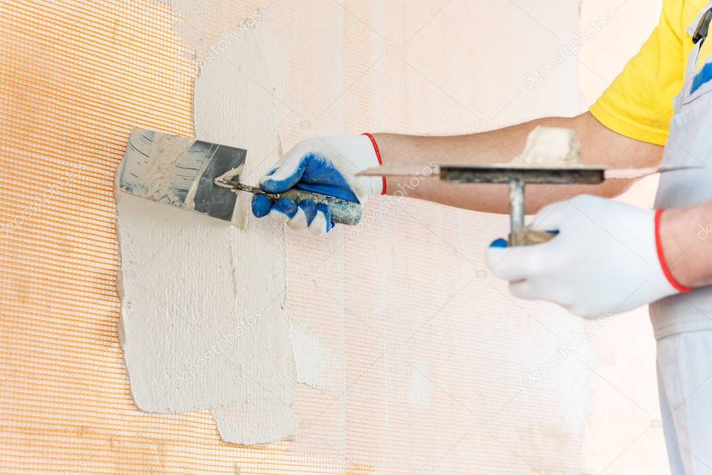 A worker is applying putty on a fiberglass mesh on the wall. He is using a trowel.