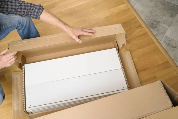 A man is unpacking a cardboard box with furniture. — Stock Photo, Image