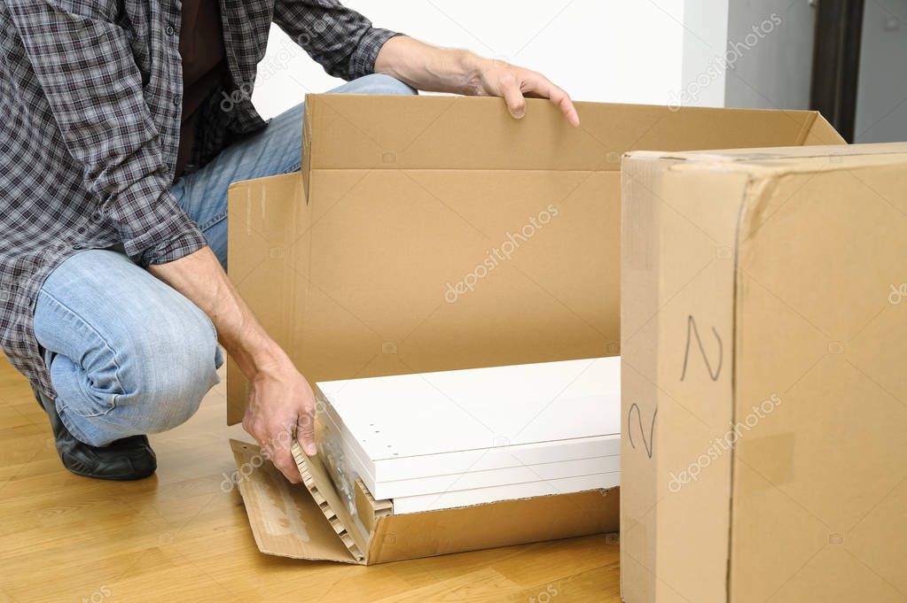 A man is unpacking a cardboard box with furniture.