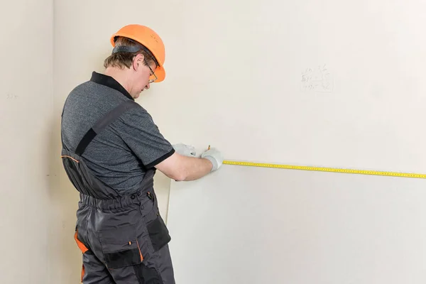 Installation of drywall. The worker is measured to cut off a piece of drywall later.